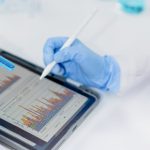 Mano con lápiz inteligente apuntado cosas en una tablet mientras con la otra mano sujeta una muestra de agua.