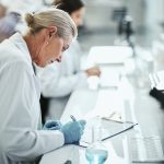 Científica rubia en un laboratorio apunta unos datos en un papel